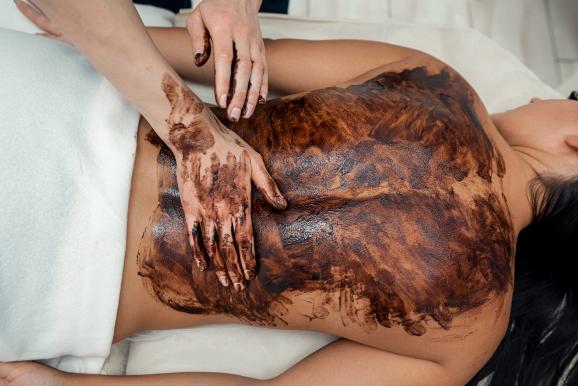 Eine weibliche Kundin liegt und lässt sich von einer Kosmetikerin mit Kakao-Schokoladen-Behandlung im Spa behandeln